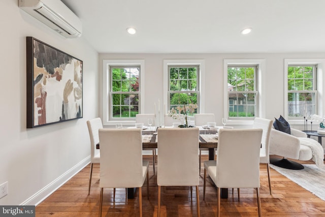 dining space featuring a healthy amount of sunlight, wood finished floors, baseboards, and a wall unit AC