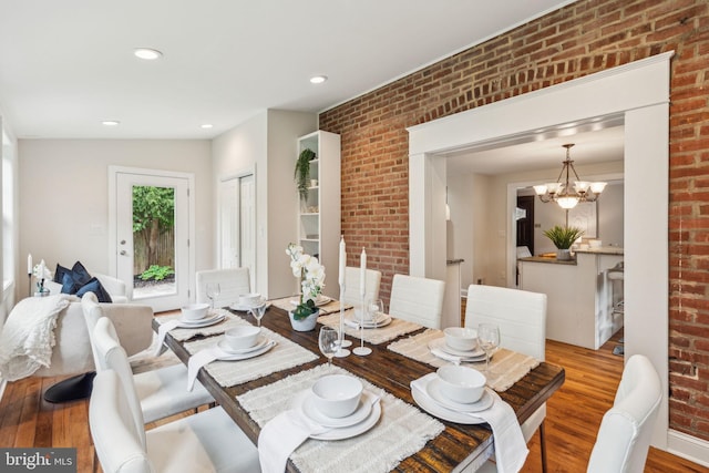 dining room featuring a notable chandelier, brick wall, recessed lighting, and wood finished floors