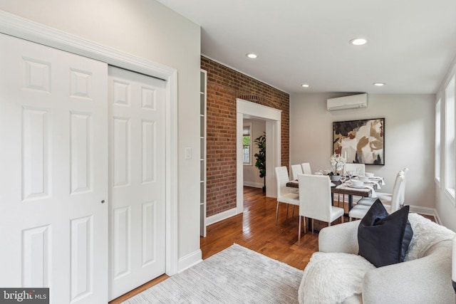 living room with wood finished floors, recessed lighting, an AC wall unit, brick wall, and baseboards