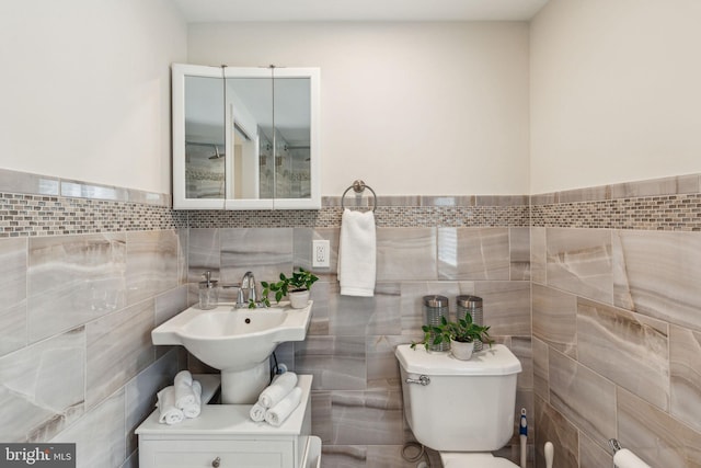 bathroom with a sink, tile walls, and toilet