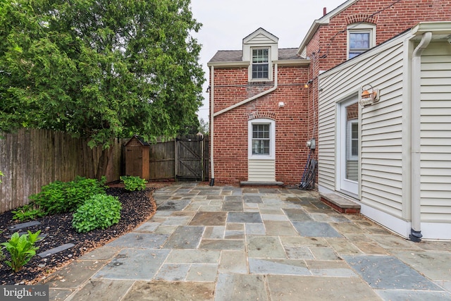 rear view of house featuring brick siding, a gate, fence, and a patio area