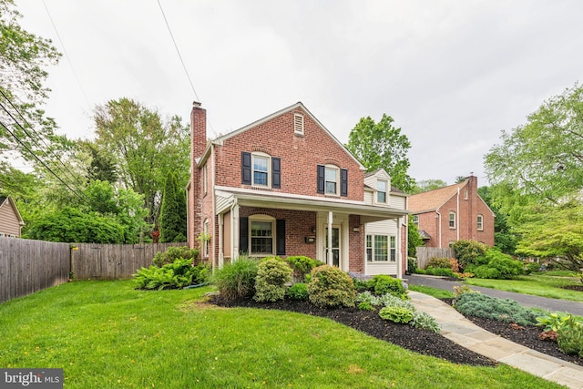 traditional-style house featuring a chimney, brick siding, a front lawn, and fence