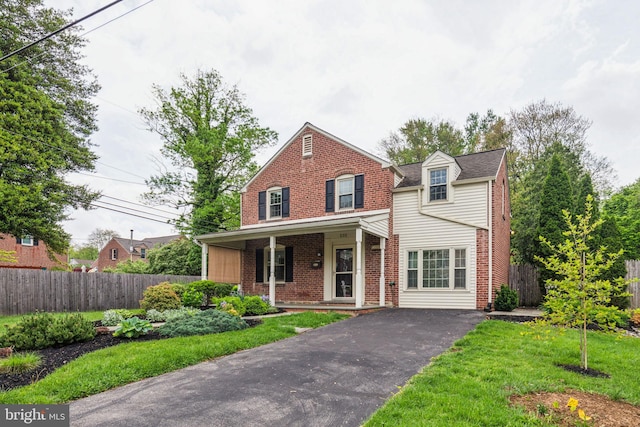 traditional-style home featuring driveway, a porch, brick siding, and fence