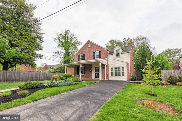 traditional-style house featuring a porch, brick siding, a front lawn, and fence