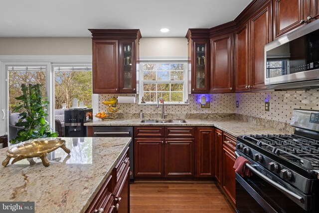 kitchen featuring a sink, tasteful backsplash, light stone counters, appliances with stainless steel finishes, and dark wood finished floors
