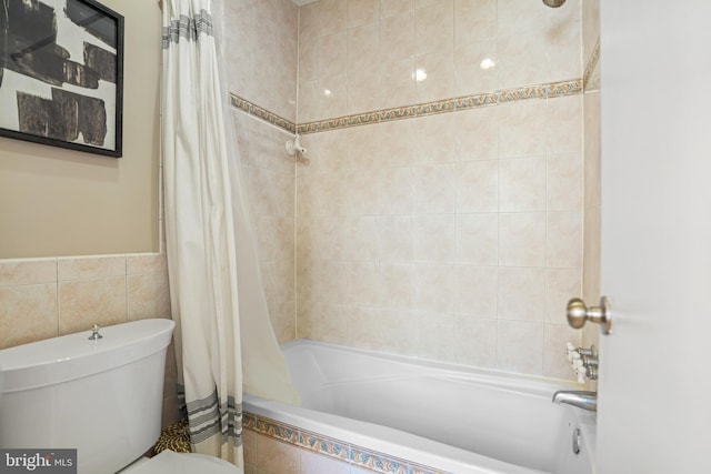 bathroom featuring tiled shower / bath combo, toilet, and tile walls