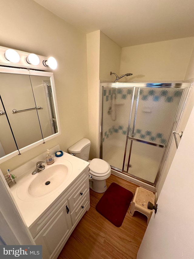 full bath with wood finished floors, a shower stall, vanity, and toilet