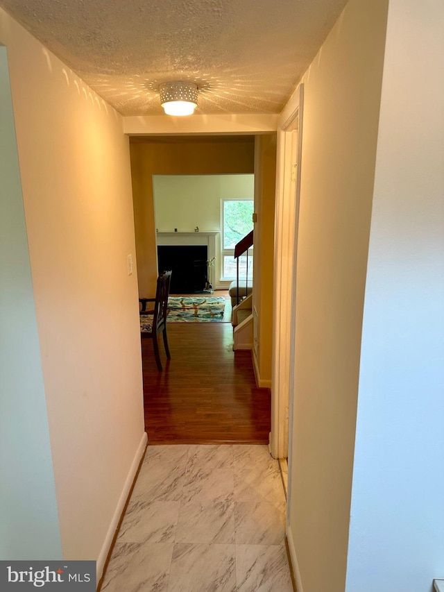 hall with light marble finish floors, a textured ceiling, baseboards, and stairs
