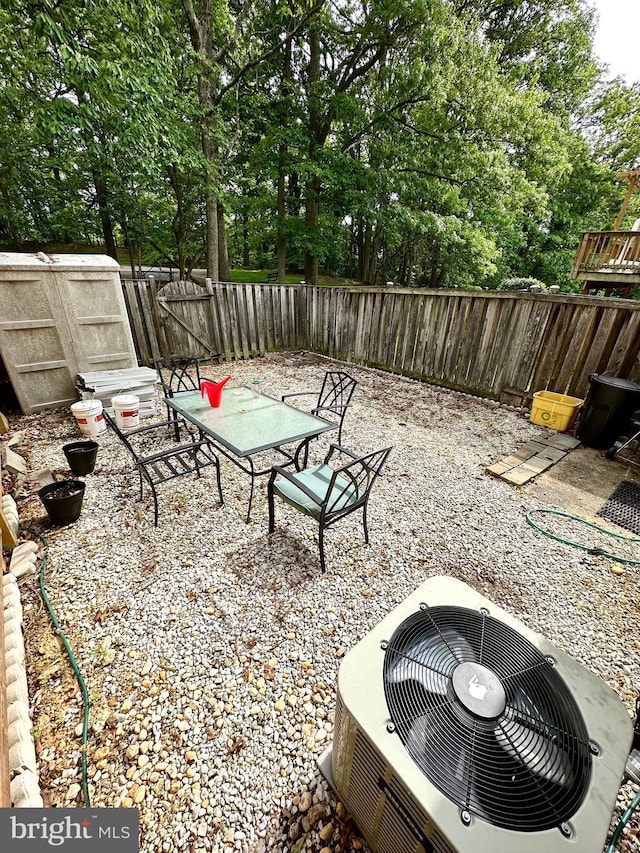 view of patio featuring cooling unit, a fenced backyard, outdoor dining area, and view of scattered trees