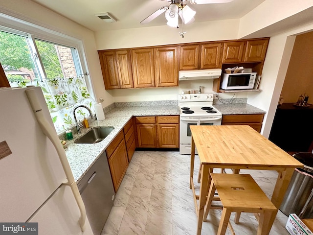 kitchen with white appliances, a sink, under cabinet range hood, brown cabinets, and light stone countertops