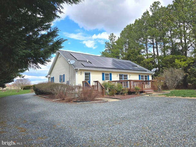 single story home featuring roof mounted solar panels and a wooden deck