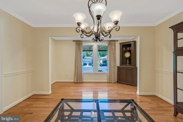 unfurnished dining area with baseboards, wood finished floors, an inviting chandelier, and crown molding