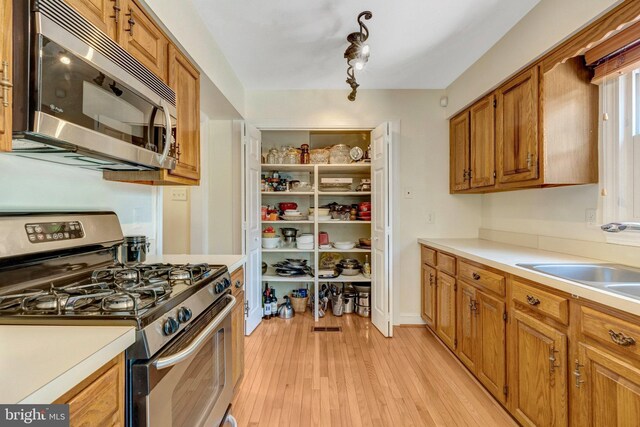 kitchen with brown cabinets, a sink, stainless steel appliances, and light countertops