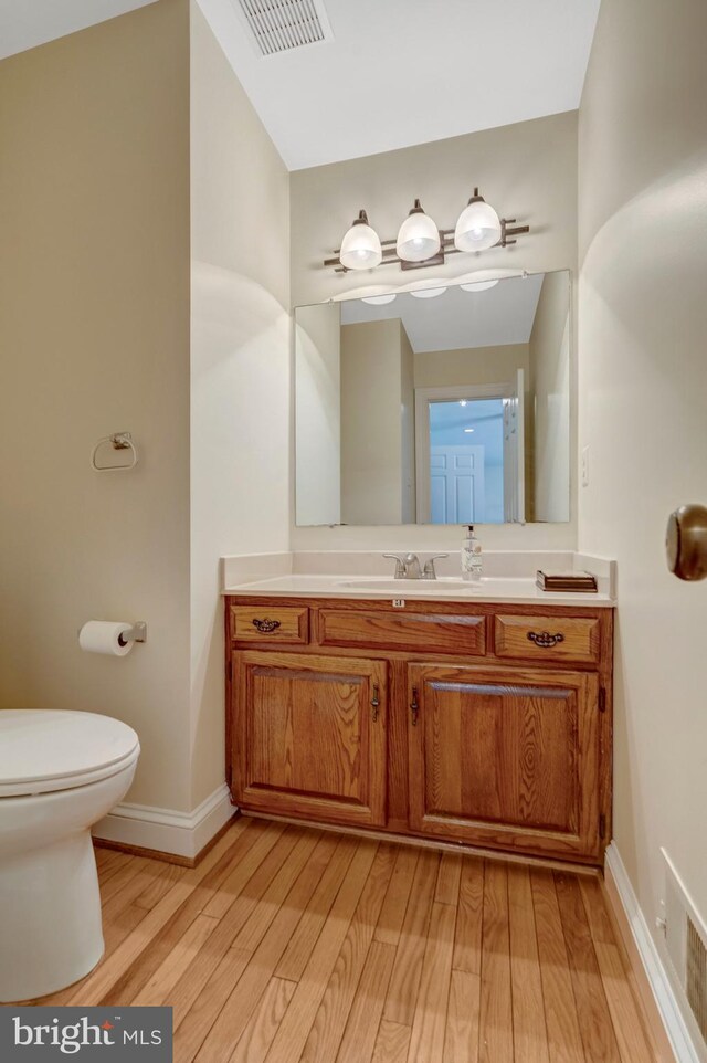 half bath featuring toilet, baseboards, visible vents, wood finished floors, and vanity