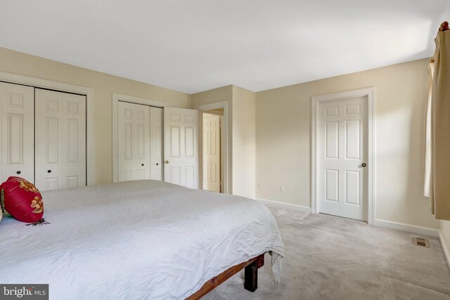 bedroom with baseboards, visible vents, two closets, and light colored carpet