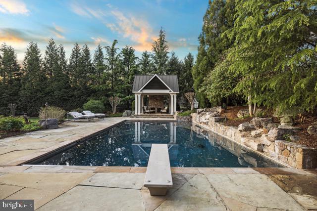 11820 Plantation Dr, Great Falls, VA 22066 - pool at dusk with a diving board, a gazebo, a patio area, and an outdoor pool