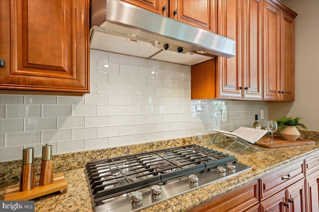 12670 Perrywood Ln, Dunkirk, MD 20754 - kitchen with stainless steel gas cooktop, under cabinet range hood, tasteful backsplash, brown cabinetry, and light stone counters