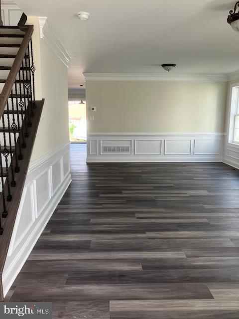 111 Heulings Ave, Riverside, NJ 08075 - unfurnished room featuring crown molding, stairs, a wainscoted wall, dark wood-style flooring, and a decorative wall