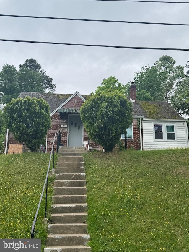 view of property hidden behind natural elements with brick siding, a chimney, and a front yard