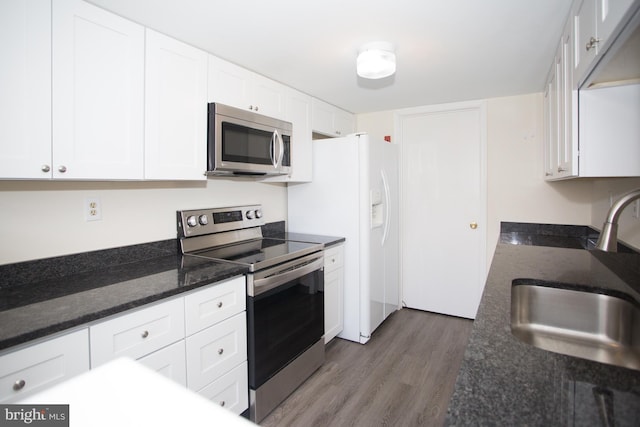 kitchen featuring a sink, wood finished floors, dark stone countertops, stainless steel appliances, and white cabinets