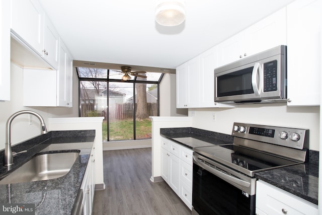 kitchen featuring white cabinetry, stainless steel appliances, dark stone counters, a sink, and a ceiling fan