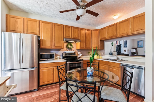 kitchen featuring under cabinet range hood, appliances with stainless steel finishes, ceiling fan, a sink, and a textured ceiling