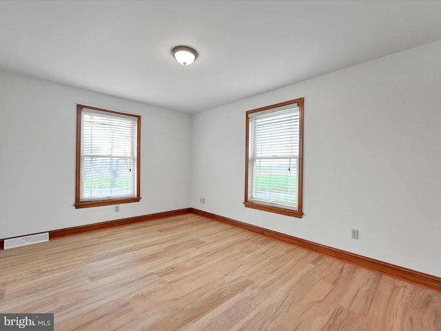 empty room with light wood finished floors, visible vents, and baseboards
