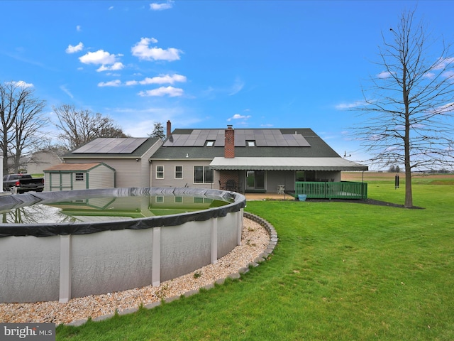 rear view of property with a chimney, roof mounted solar panels, a covered pool, and a lawn
