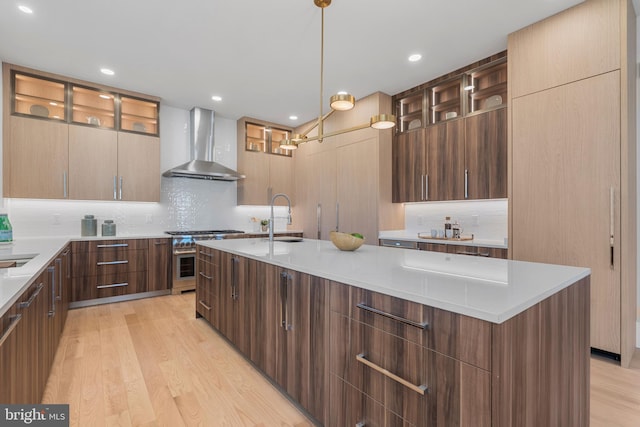 kitchen with a sink, modern cabinets, wall chimney range hood, and light wood-style floors