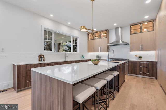 kitchen with a sink, wall chimney exhaust hood, modern cabinets, a kitchen island with sink, and visible vents
