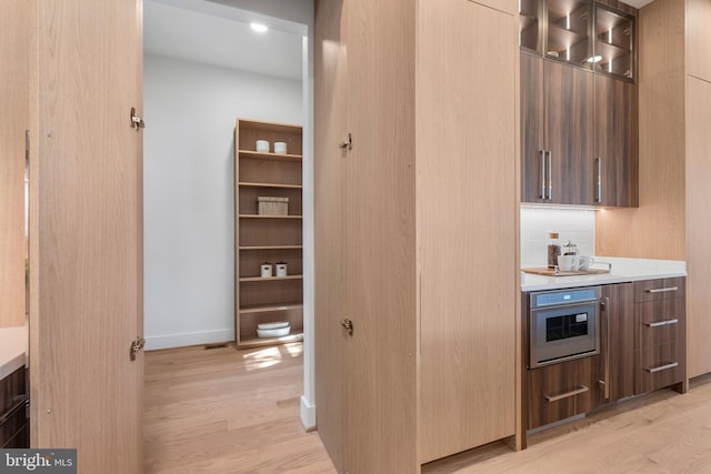 kitchen with light wood finished floors, modern cabinets, wall oven, and light countertops