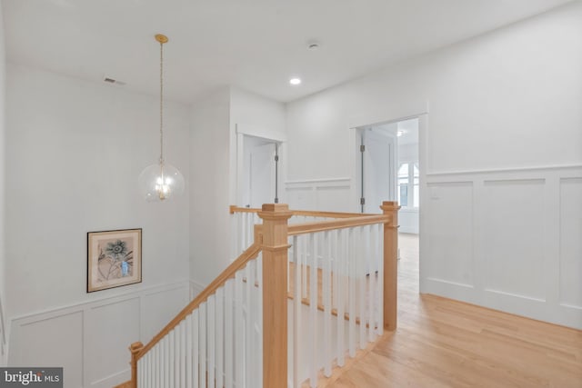 hallway featuring an upstairs landing, a decorative wall, recessed lighting, light wood-type flooring, and a notable chandelier