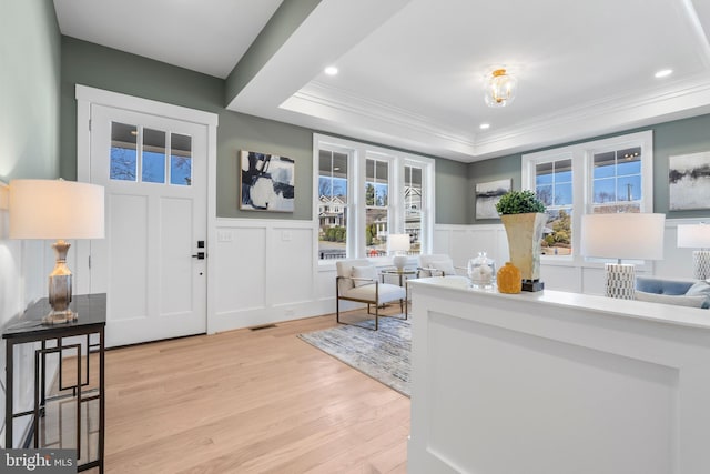 foyer with light wood-type flooring, a raised ceiling, ornamental molding, and wainscoting