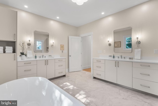 full bathroom featuring marble finish floor, a soaking tub, a sink, and two vanities