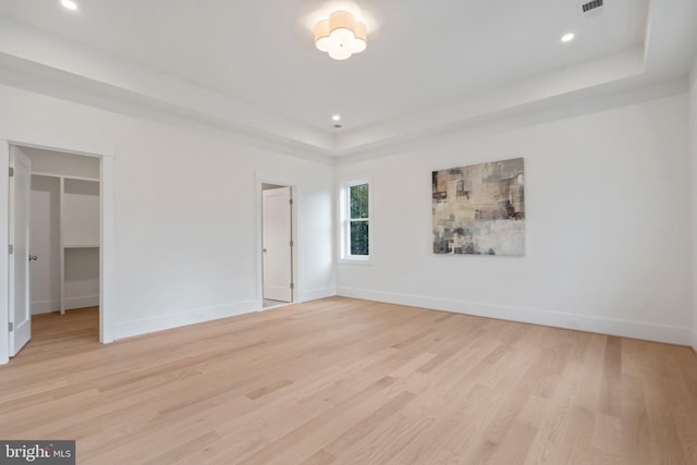 interior space with a raised ceiling, light wood finished floors, baseboards, visible vents, and recessed lighting
