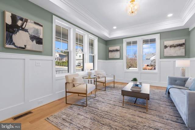 sitting room with a tray ceiling, ornamental molding, visible vents, a decorative wall, and wood finished floors