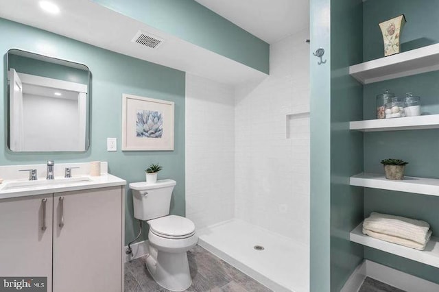 bathroom featuring vanity, toilet, visible vents, tiled shower, and wood finished floors
