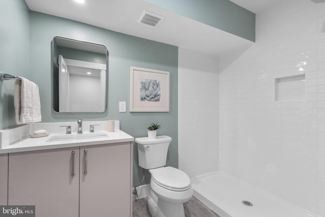 full bath featuring visible vents, a tile shower, toilet, wood finished floors, and vanity