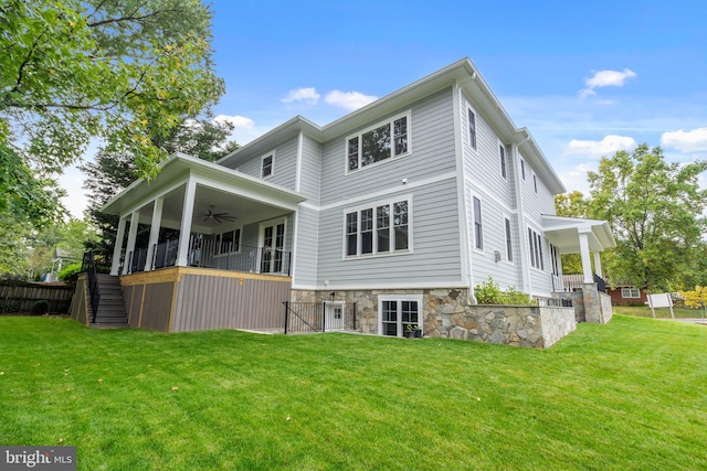 back of house featuring a yard, stone siding, stairway, and a ceiling fan