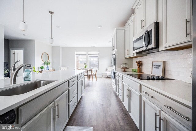 kitchen with stainless steel microwave, light countertops, dark wood-type flooring, decorative backsplash, and a sink