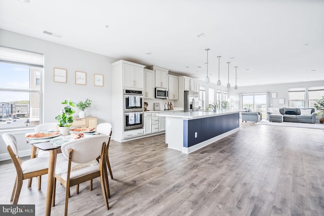 kitchen featuring open floor plan, an island with sink, light countertops, stainless steel appliances, and light wood finished floors