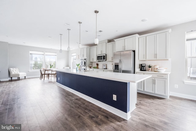 kitchen featuring appliances with stainless steel finishes, a sink, light countertops, a center island with sink, and light wood finished floors