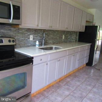 912 N Fremont Ave, Baltimore, MD 21217 - kitchen with decorative backsplash, light tile patterned floors, appliances with stainless steel finishes, light countertops, and a sink