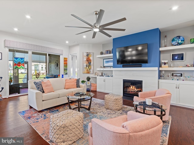 living area with a ceiling fan, a glass covered fireplace, dark wood-style floors, built in features, and recessed lighting
