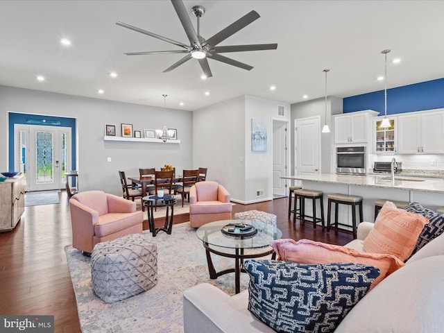 living area featuring dark wood-type flooring, visible vents, recessed lighting, and ceiling fan with notable chandelier