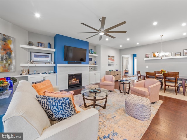 living room featuring ceiling fan with notable chandelier, a tiled fireplace, wood finished floors, and recessed lighting