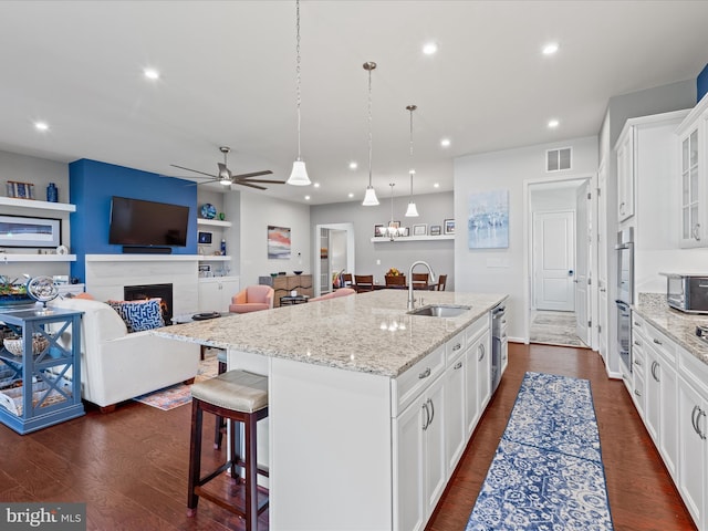 kitchen with a sink, white cabinetry, a center island with sink, dark wood-style floors, and ceiling fan