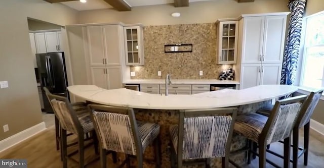 kitchen featuring backsplash, black fridge, a large island, baseboards, and white cabinets