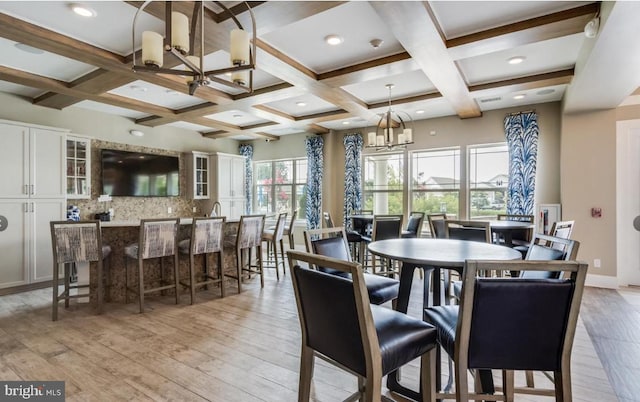 dining space featuring light wood-style flooring, coffered ceiling, a notable chandelier, and beam ceiling