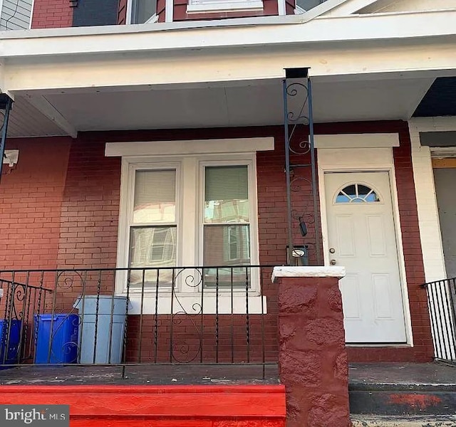 view of exterior entry with brick siding and covered porch